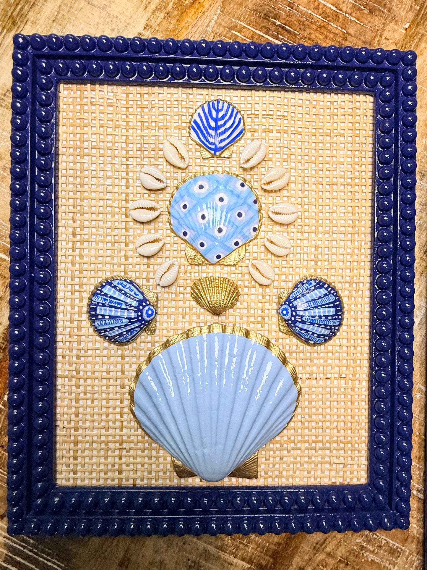 Decorative wall art with blue and gold shell designs on a woven background, framed in blue.
