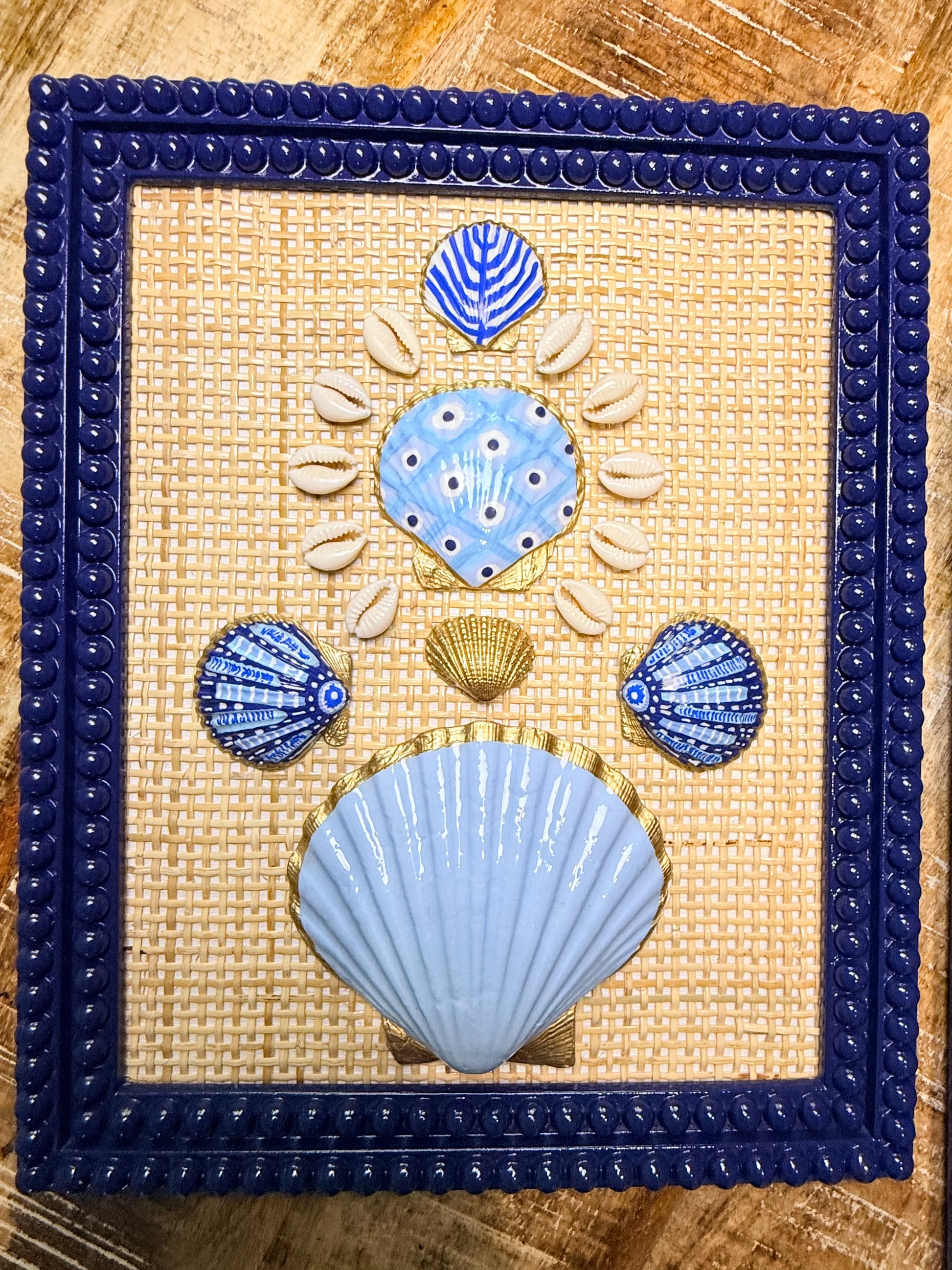 Decorative wall art with blue and gold shell designs on a woven background, framed in blue.